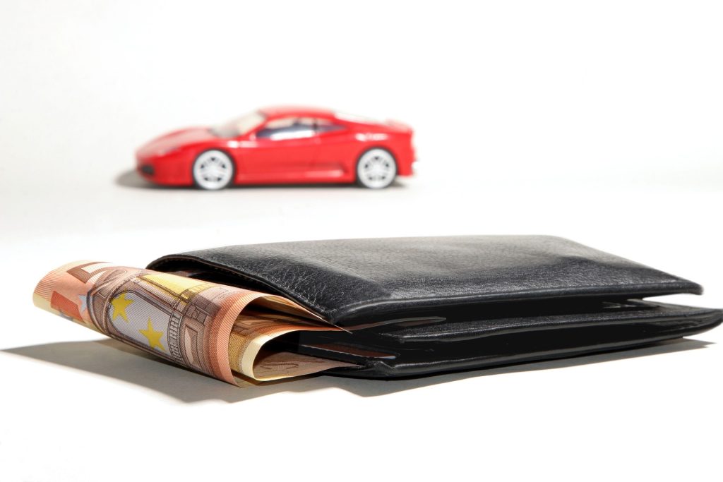An upclose image of a wallet with money inside and a red car in the background.