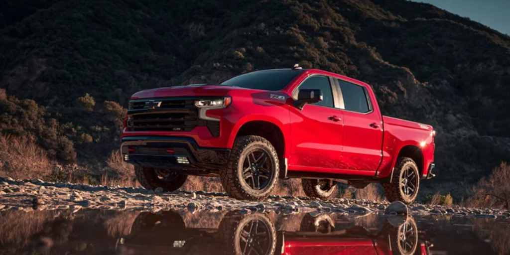A red 2023 Chevrolet Silverado driving through muddy waters.