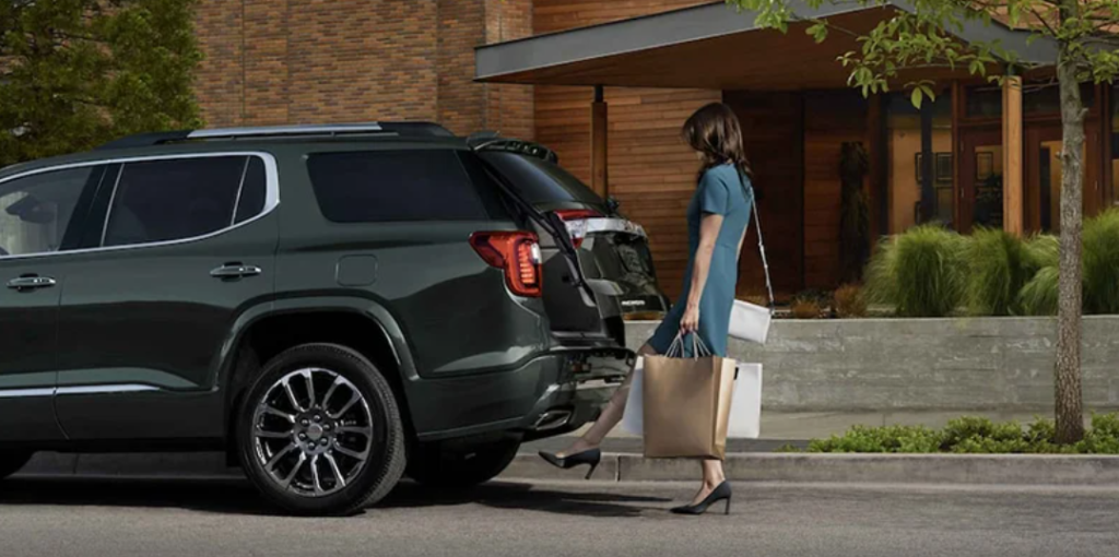 A woman using the foot-lift gate to open the trunk of her 2023 GMC Acadia.