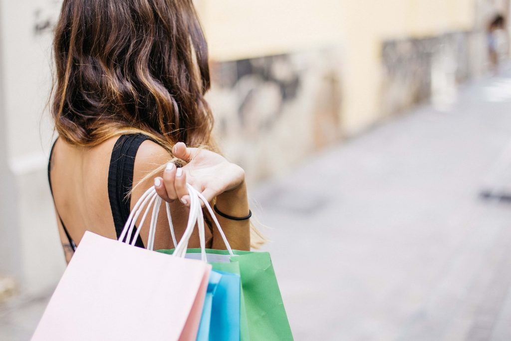 A woman holding three shopping bags that are pink, green, and blue.