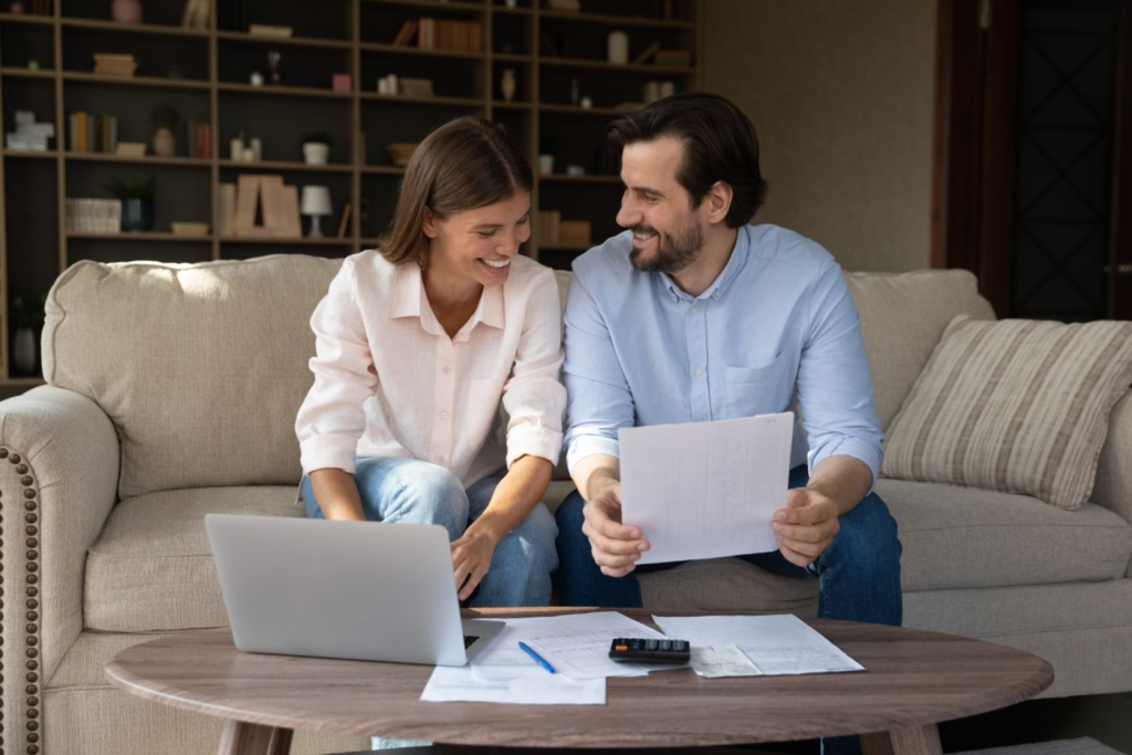 A couple sitting on a couch, reviewing documents together with a laptop and calculator on the table.