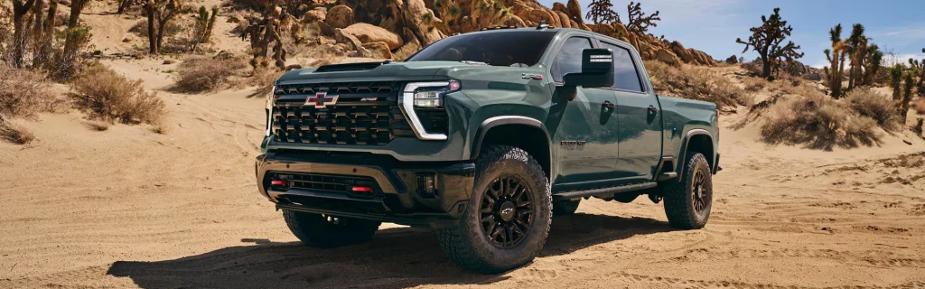 A Chevrolet Silverado ZR2 pickup truck driving through a desert landscape with rugged terrain and sparse vegetation.