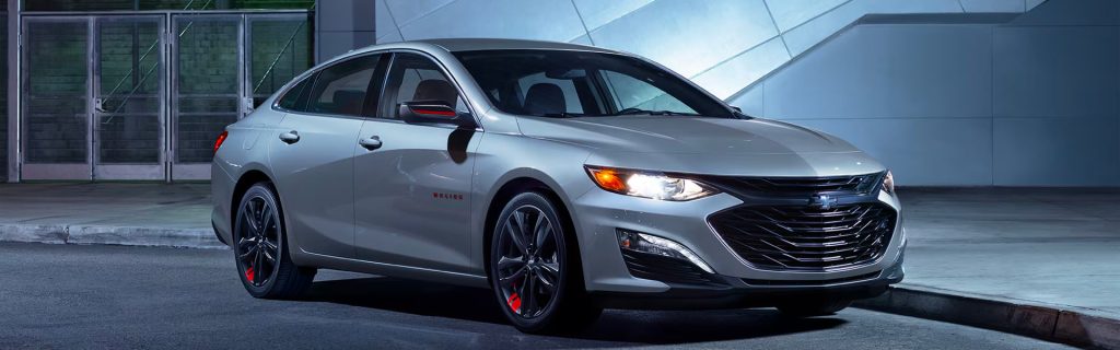 Silver Chevrolet Malibu sedan parked outside a modern building
