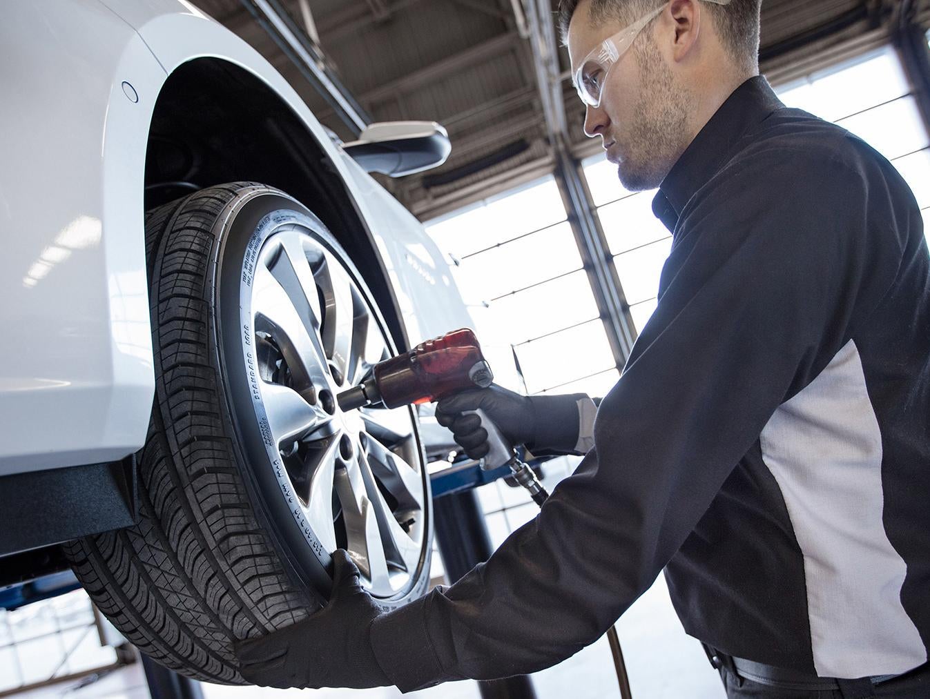 Technician uses a power tool to service a car’s wheel.